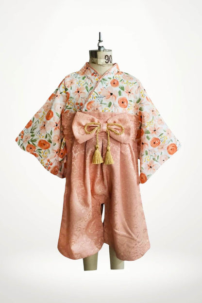 Yukata pour bébé avec motifs floraux roses et un nœud doré, sur un mannequin au fond blanc