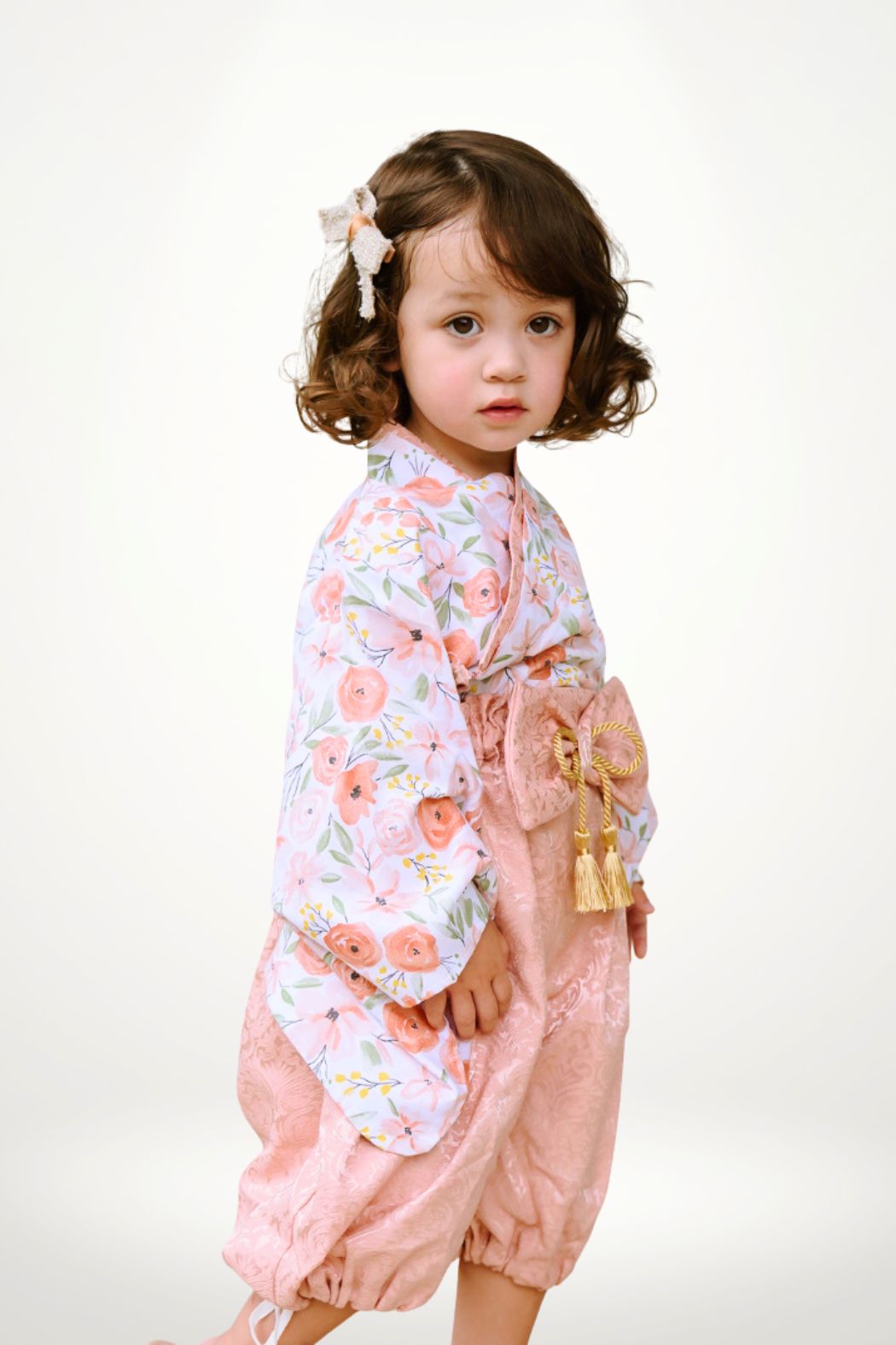 Une petite fille porte un yukata à fleurs roses, avec un pantalon bouffant et un nœud dans les cheveux