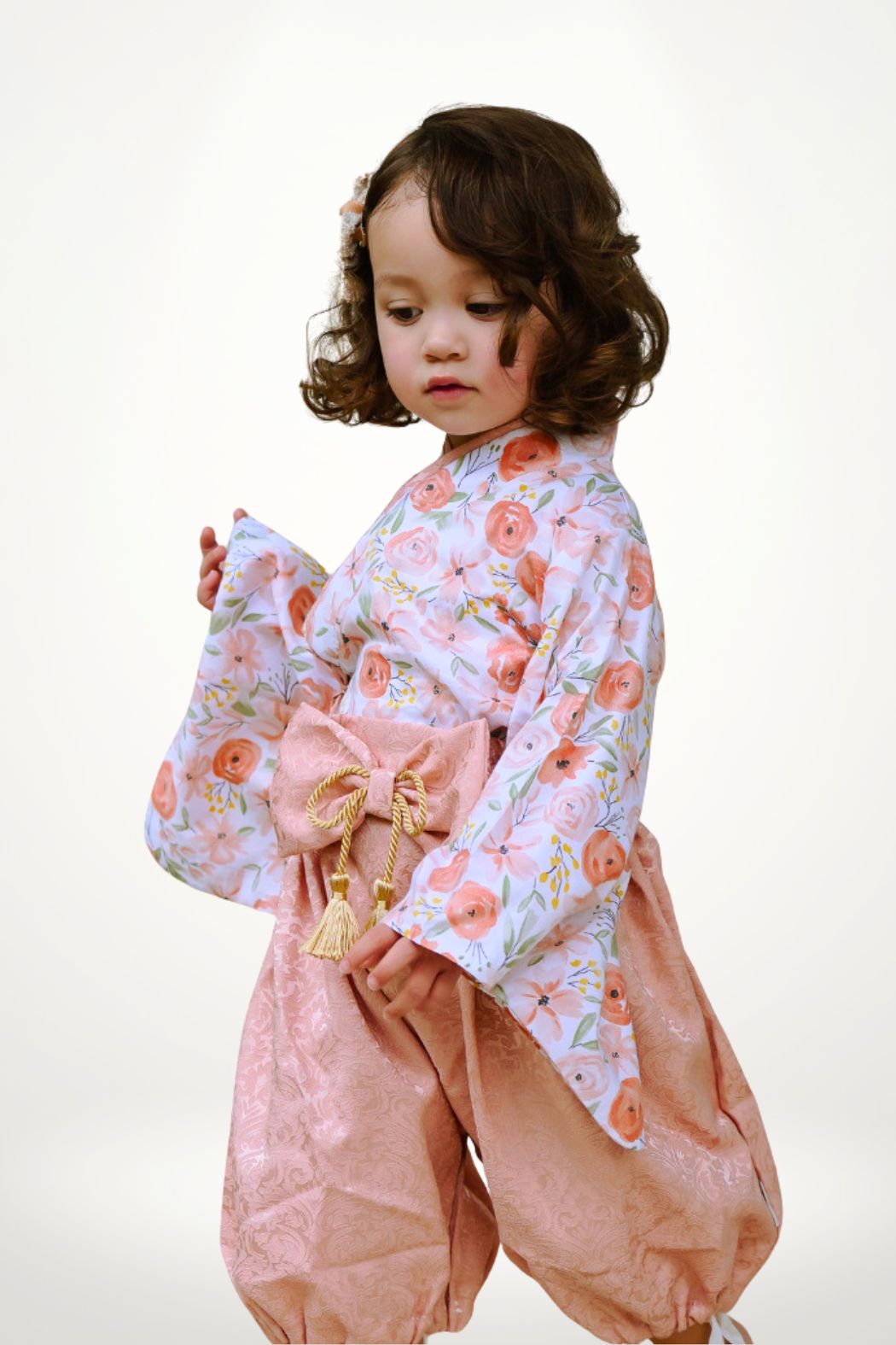 Enfant portant un yukata à fleurs roses, avec un pantalon rose et un nœud élégant, sur fond neutre