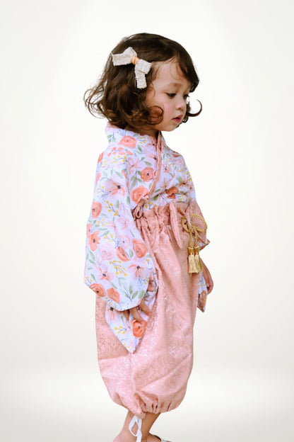Une petite fille en yukata aux motifs floraux roses, avec un pantalon rose et un nœud dans les cheveux