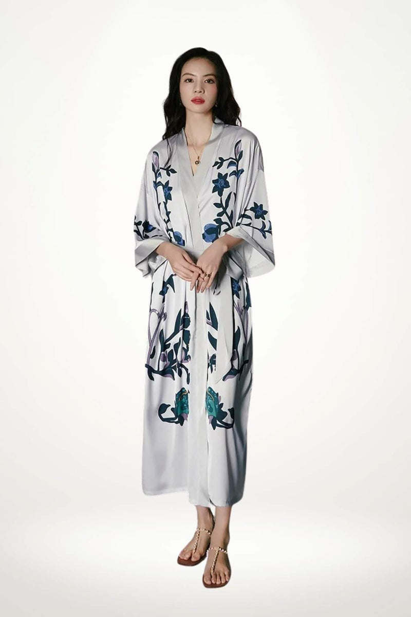 Kimono blanc orné de motifs floraux bleus, porté par une femme aux cheveux longs, fond neutre