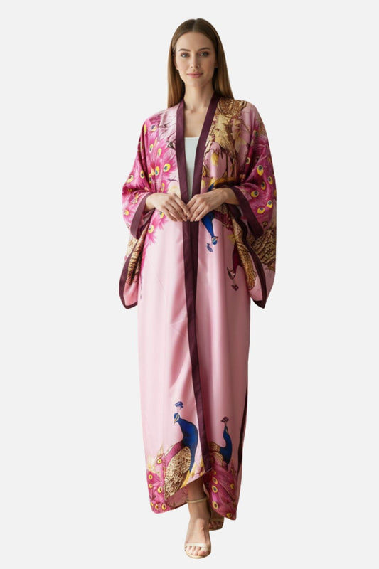 Femme en kimono chic rose avec motifs de paons, posant avec élégance sur fond neutre