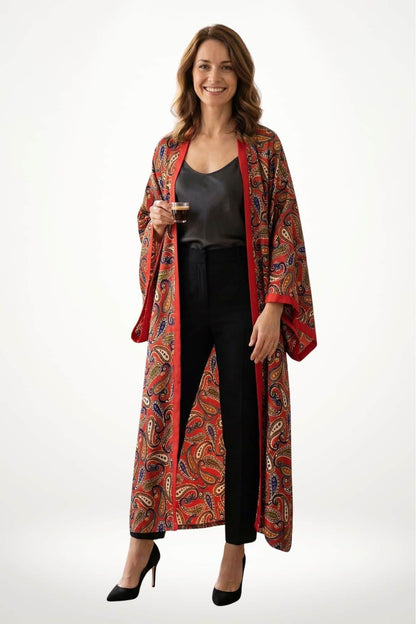 Femme souriante portant un kimono rouge à motifs paisley, avec un top noir et un pantalon noir, tenant une tasse