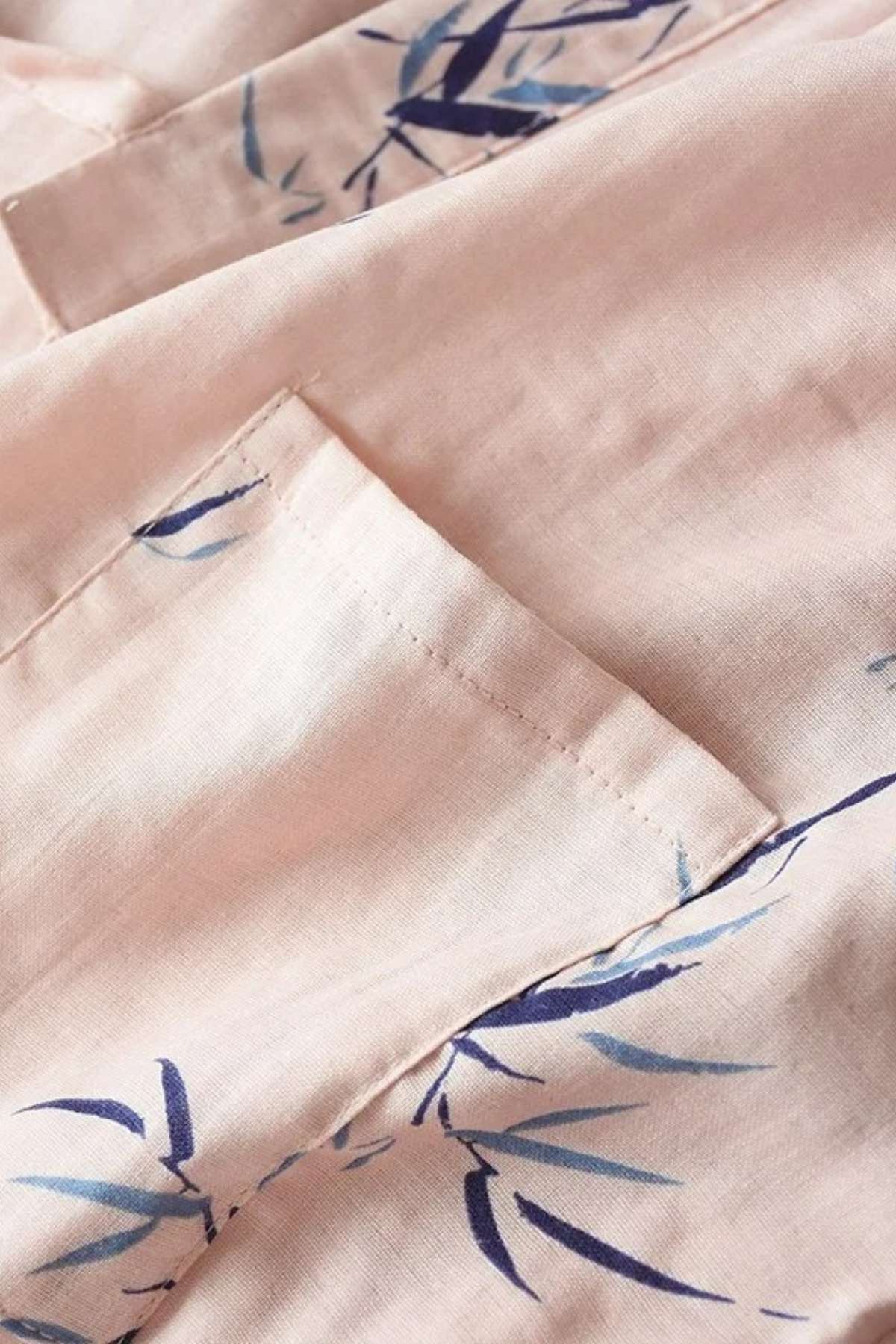 Tissu en coton rose clair avec motifs de feuilles bleues, montrant une texture douce et légère