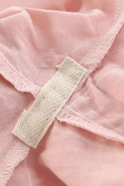 Zoom sur un tissu en coton rose avec des coutures délicates et une étiquette beige, évoquant un kimono élégant