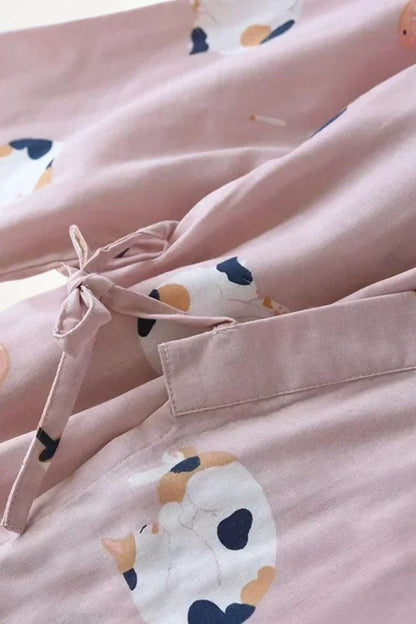 Kimono en coton rose avec des motifs de chats colorés, noué à la taille et drapé sur un fond doux