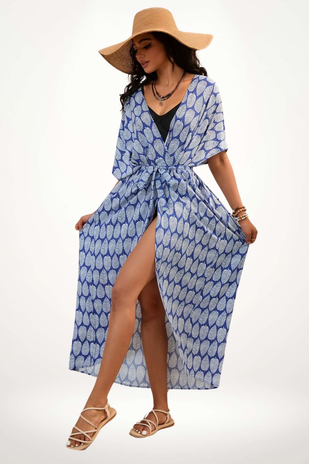 Kimono de plage bleu avec motifs de feuilles blanches, porté par une femme en sandales, sous un grand chapeau