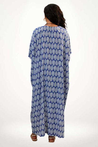 Kimono de plage bleu à motifs de feuilles blanches, porté par une femme aux cheveux bouclés, sur fond blanc