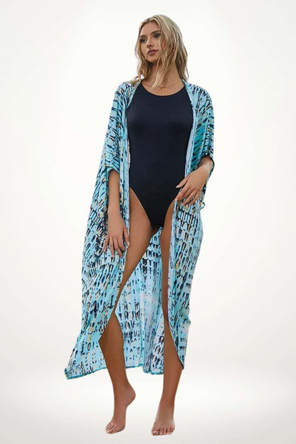 Kimono de plage bleu clair à motifs fluides, porté ouvert sur un maillot noir, avec une posture élégante