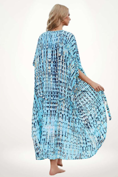 Kimono de plage fluide aux motifs bleus et beiges, porté par une femme debout, décor sobre en arrière-plan