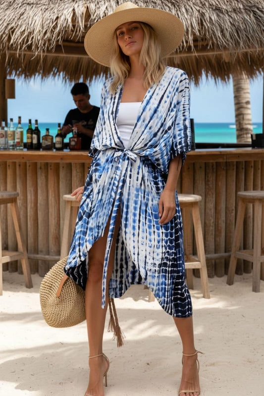 Femme portant un kimono bleu et blanc avec un chapeau, se tenant devant un bar en bois sur la plage
