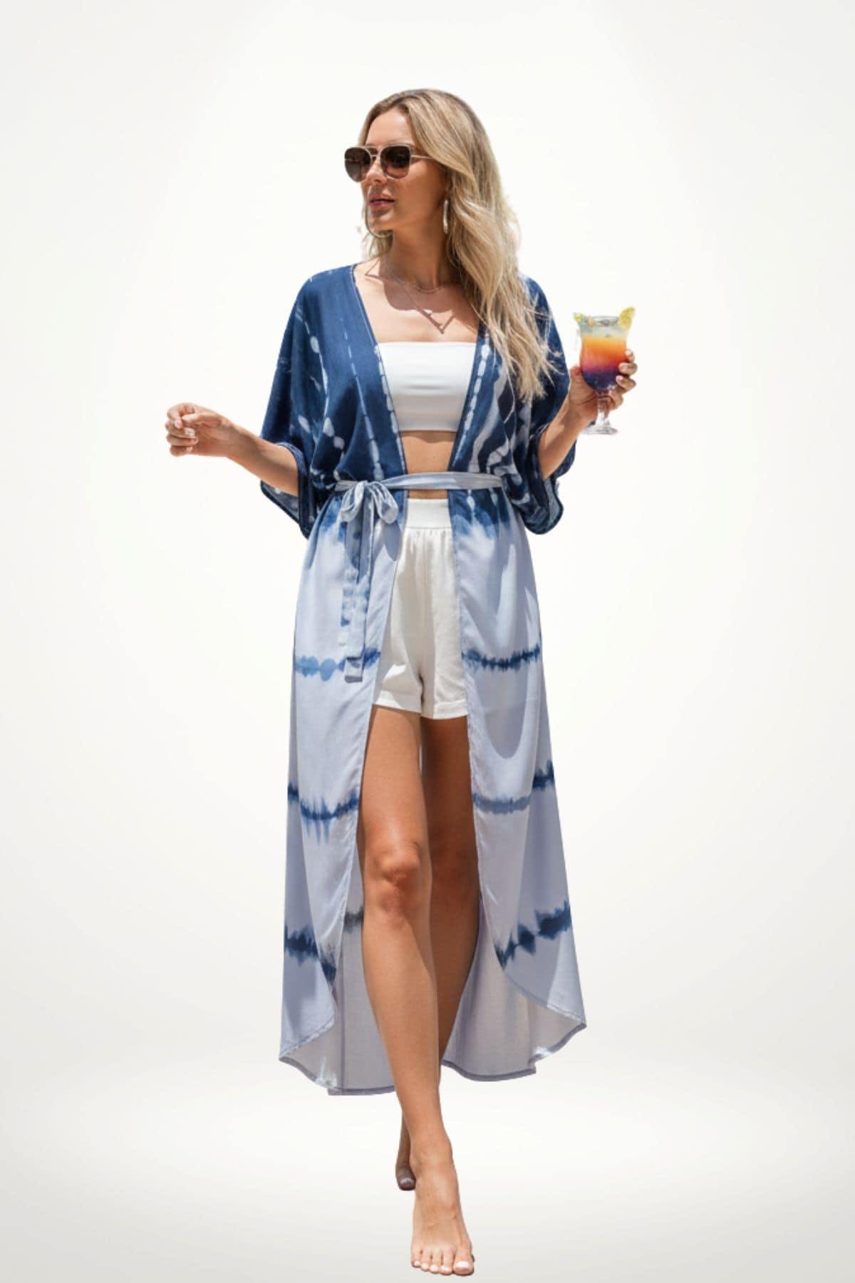 Femme en kimono bleu à motifs tie-dye, portant un haut blanc et un short, tenant un cocktail coloré