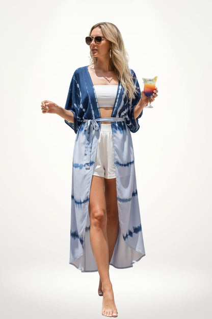 Femme en kimono bleu à motifs tie-dye, portant un haut blanc et un short, tenant un cocktail coloré