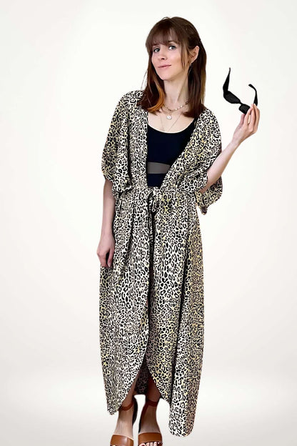 Femme portant un kimono à motifs léopard, avec des sandales marron et des lunettes de soleil dans la main