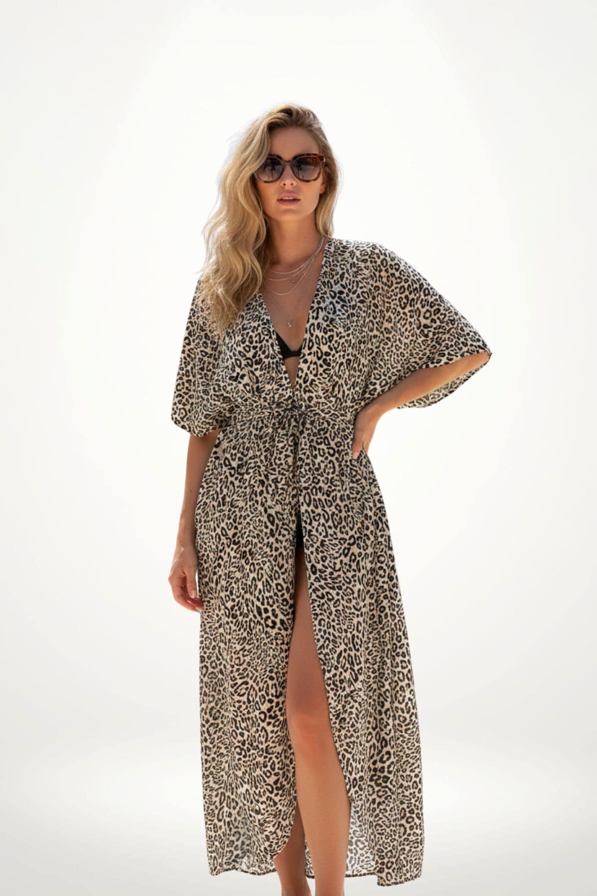Femme portant un kimono à motifs léopard, avec des lunettes de soleil, sur fond blanc lumineux