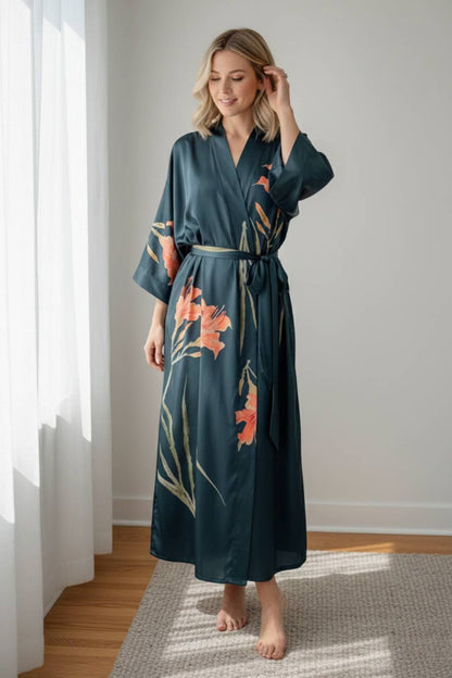 Kimono long en satin vert avec des motifs floraux orange, porté par une femme souriante dans un intérieur lumineux