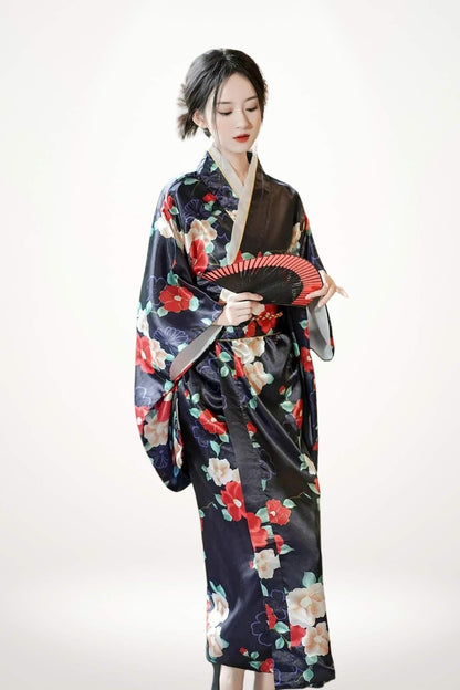 Femme en kimono satin noir à motifs floraux colorés, tenant un éventail rouge, sur fond neutre