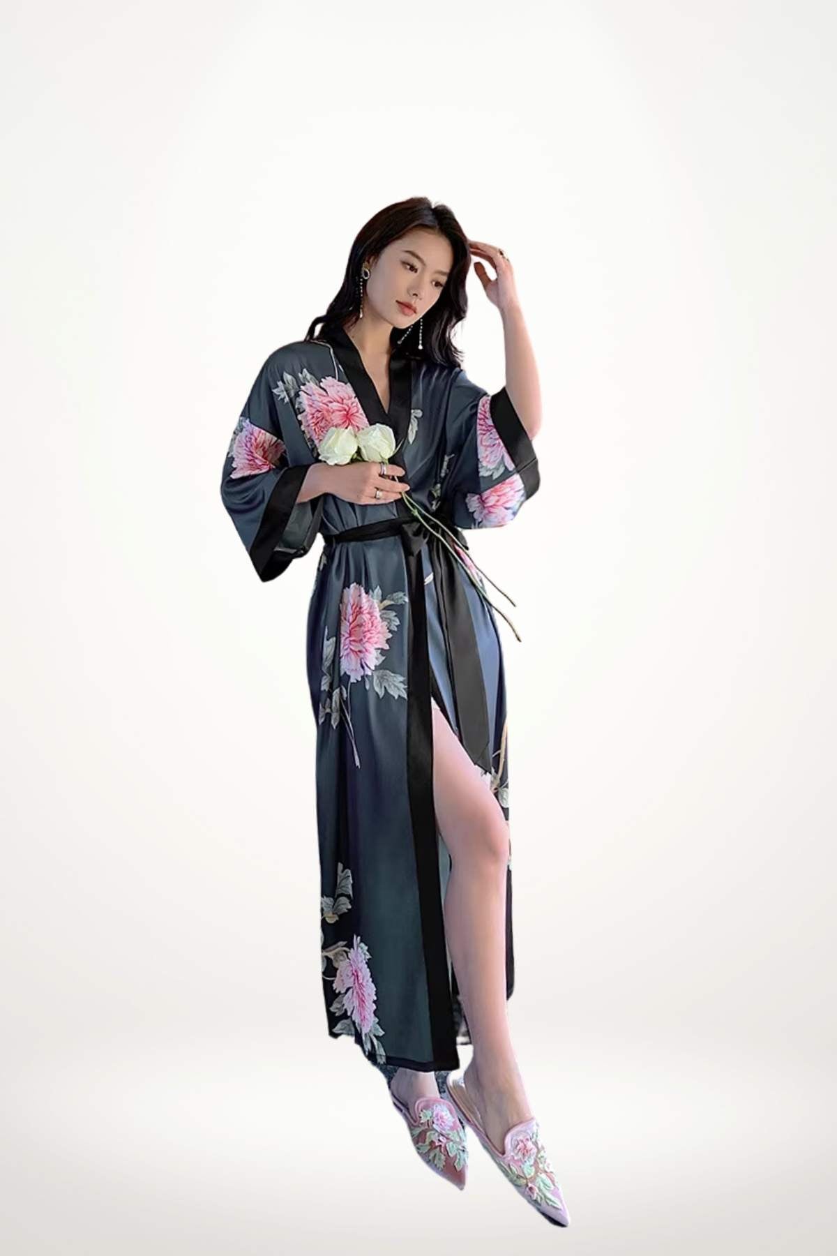 Femme en kimono en satin noir avec motifs floraux roses, posant élégamment avec des fleurs blanches