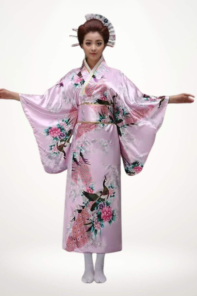 Femme en kimono long rose en satin orné d’un motif de paon et de fleurs délicates.
