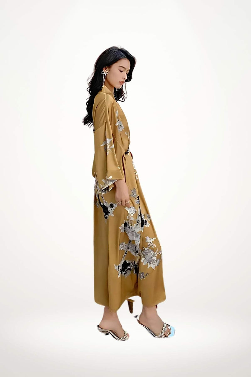 Femme en kimono satin doré avec motifs floraux, posant en profil sur fond neutre