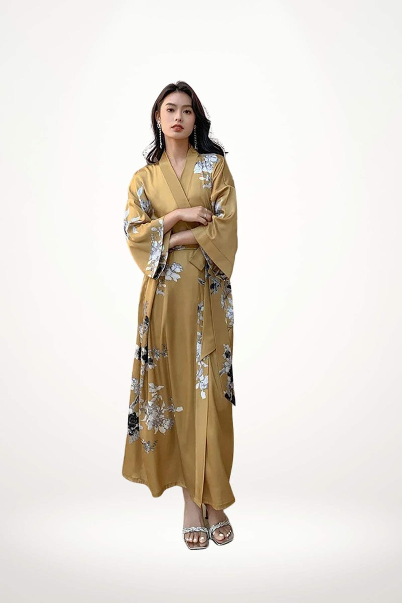Femme en kimono en satin doré avec motifs floraux, posant élégamment sur fond neutre
