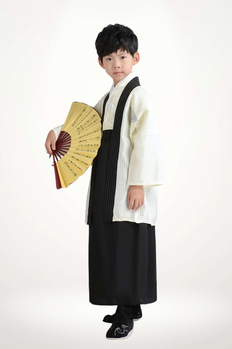 Un enfant porte un kimono traditionnel japonais blanc et noir, tenant un éventail jaune avec des motifs
