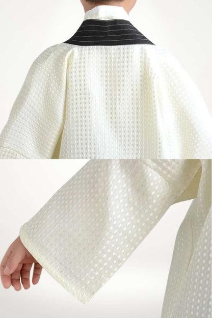 Kimono enfant en tissu blanc avec motifs en relief, col noir et manches larges, sur fond neutre