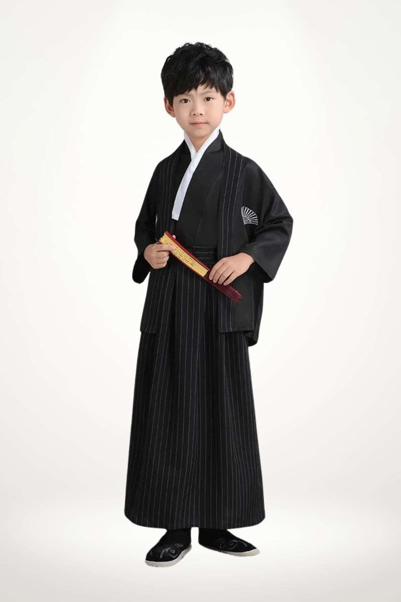 Un enfant porte un kimono noir à rayures avec un col blanc et des chaussons noirs, se tenant droit