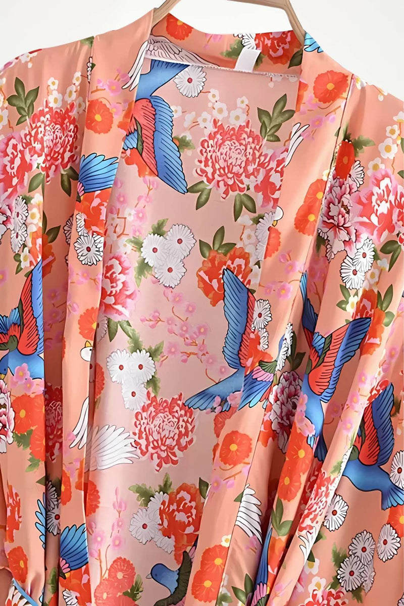 Kimono léger aux motifs floraux colorés, dominé par des teintes roses, bleues et blanches, suspendu sur un cintre