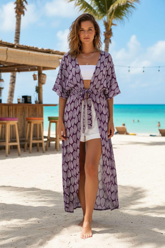 Femme en kimono violet à motifs feuilles, debout sur la plage, avec un décor tropical en arrière-plan