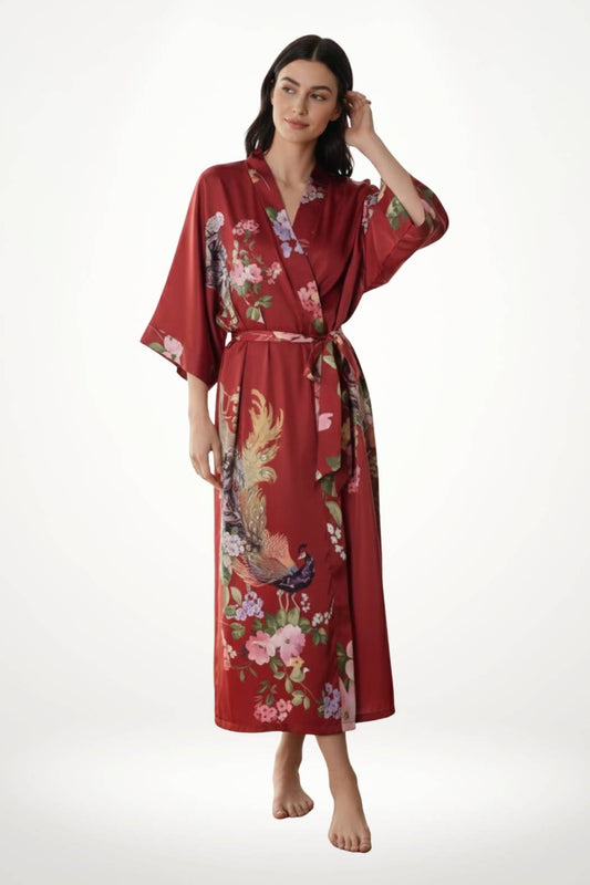 Femme portant un kimono long satiné rouge avec des motifs floraux colorés, se tenant debout dans une posture élégante