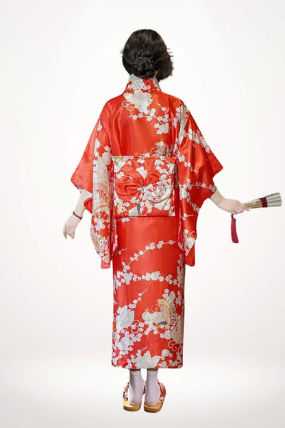Femme en kimono rouge brillant avec motifs floraux, tenant un éventail, vue de dos sur fond clair