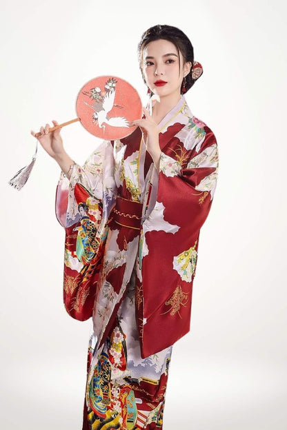 Femme portant un kimono long rouge en satin avec motifs de géisha et pagodes, ceinture obi nœud papillon, élégance traditionnelle japonaise.
