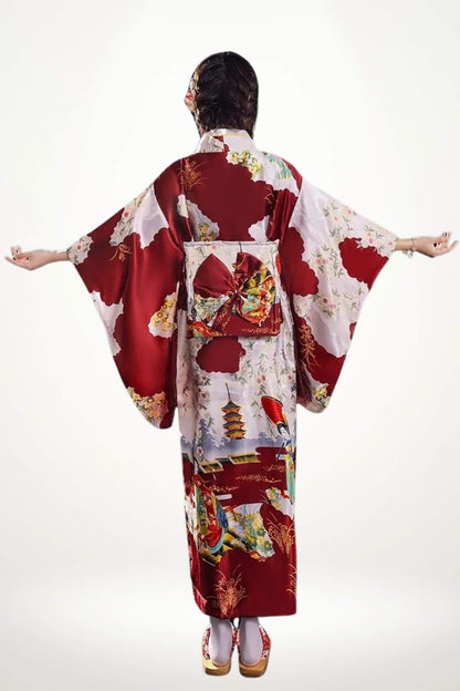 Femme de dos portant un kimono rouge avec motifs floraux et pagodes, bras écartés dans un décor minimaliste