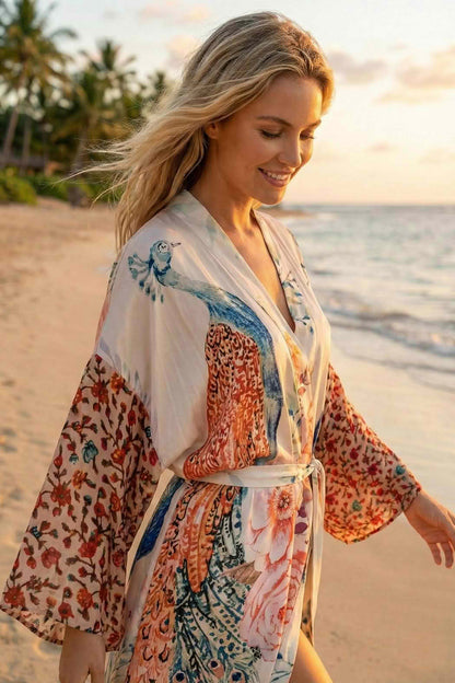 Femme souriante portant un kimono en satin aux motifs floraux et colorés, marchant sur la plage au coucher du soleil