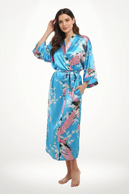 Kimono en satin bleu vif avec motifs floraux roses et oiseaux, porté par une femme souriante en posture décontractée