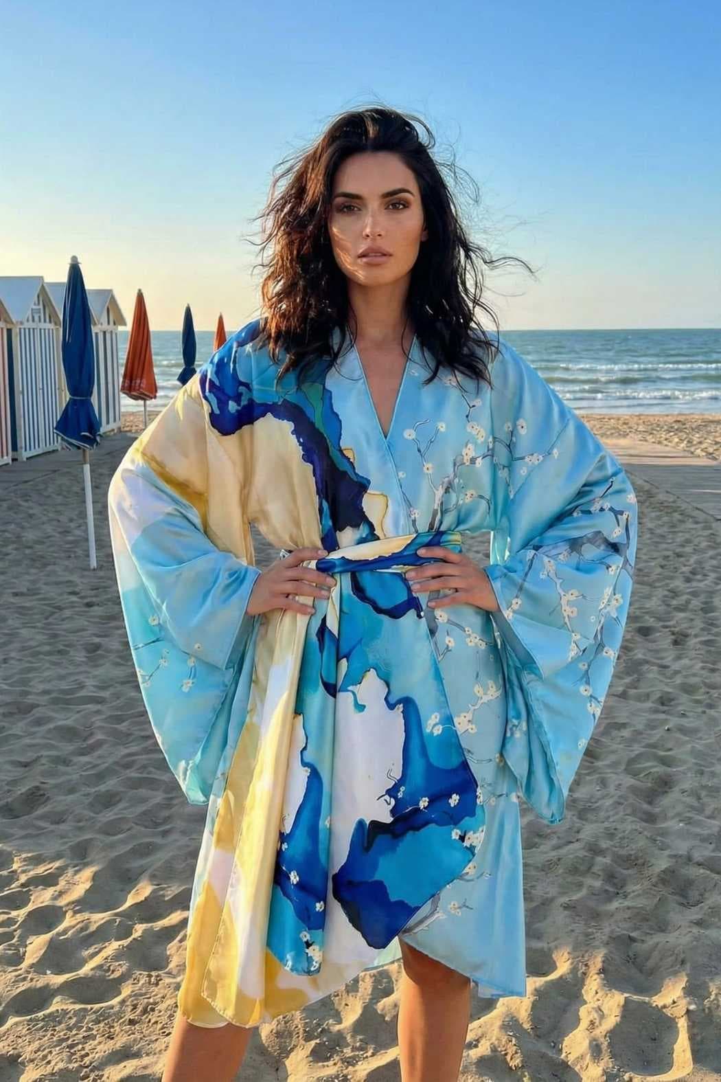 Femme portant un kimono bleu aux motifs aquatiques, se tenant sur la plage avec des parasols colorés en arrière-plan