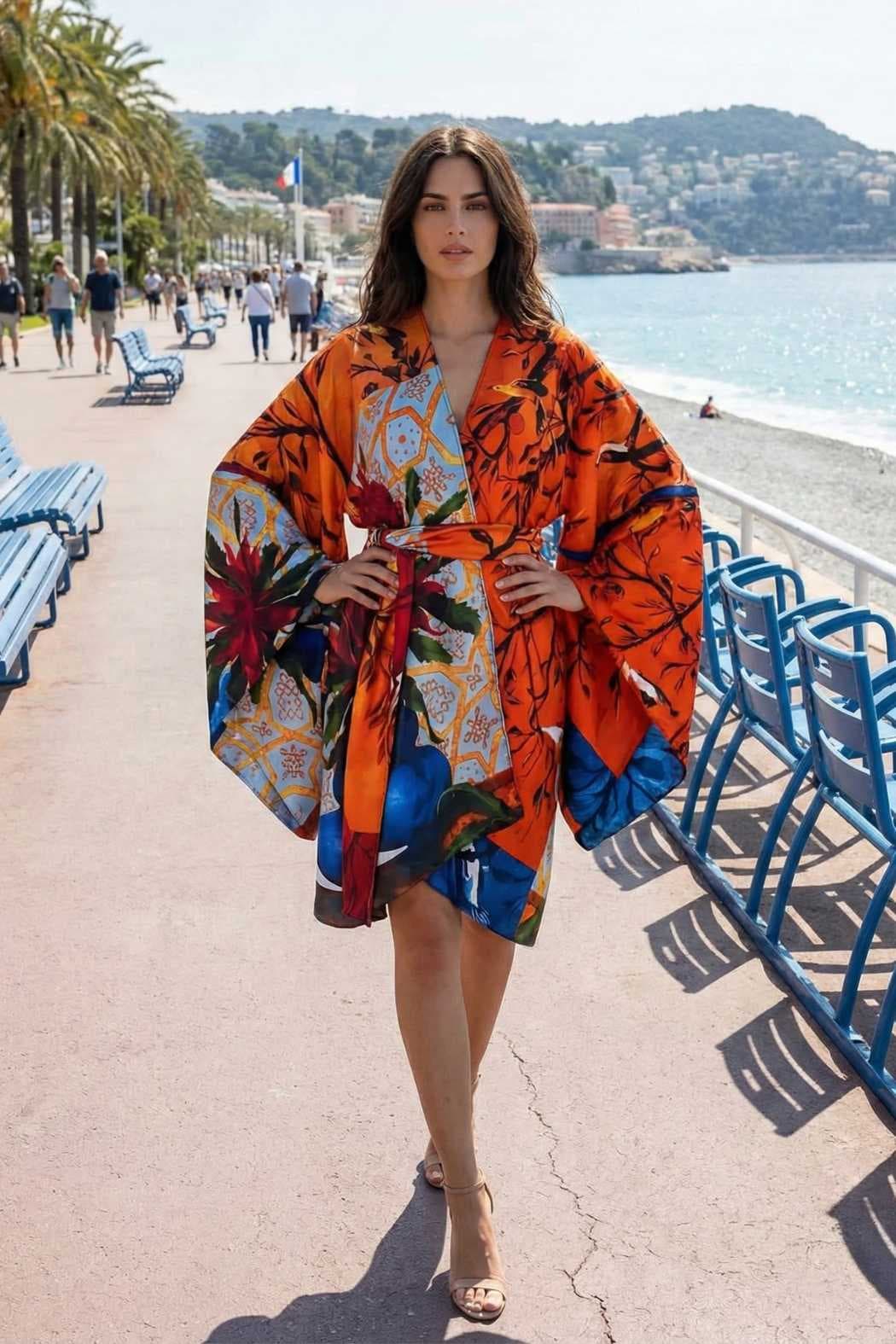 Femme en kimono coloré orange avec motifs floraux, posant sur une promenade en bord de mer ensoleillée