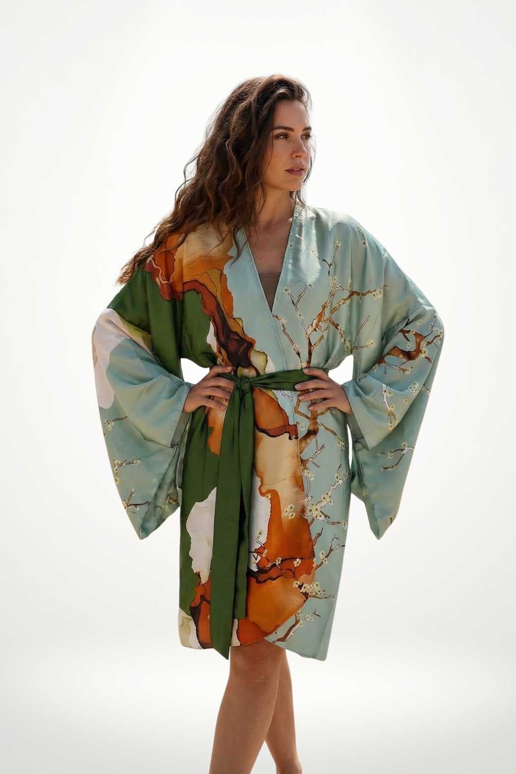 Femme portant un kimono aux couleurs douces, motifs floraux et ceinture verte, posant avec élégance sur fond clair