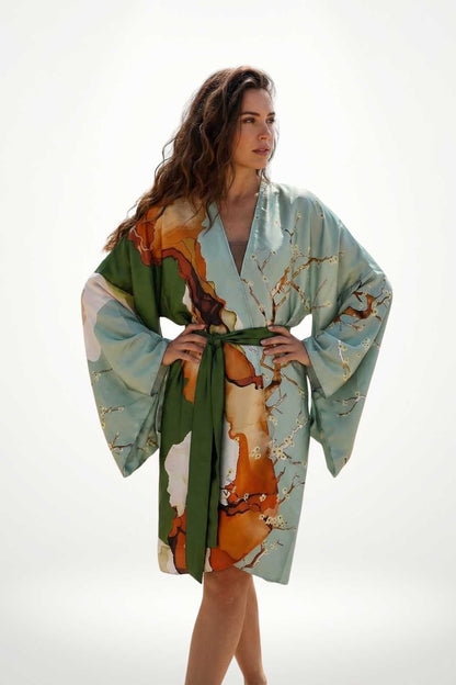 Femme portant un kimono aux couleurs douces, motifs floraux et ceinture verte, posant avec élégance sur fond clair