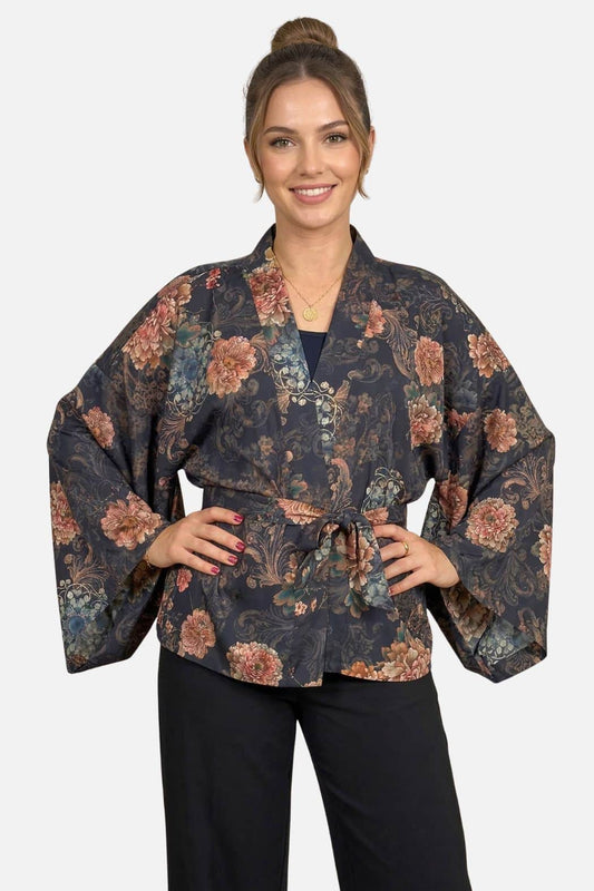 Femme souriante portant un kimono à fleurs sombres dans un décor minimaliste, avec des manches larges et une ceinture