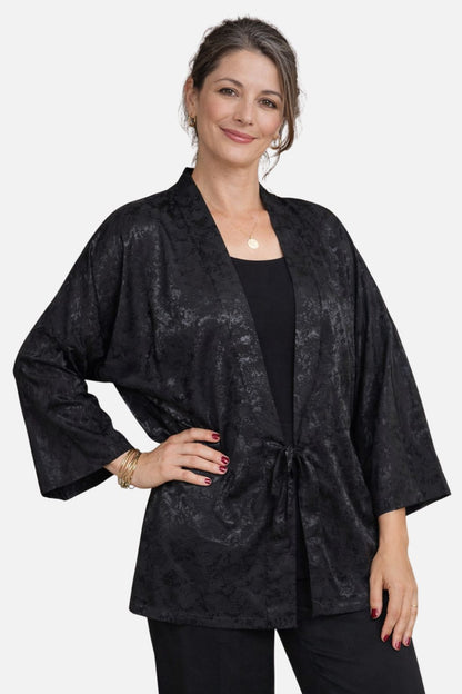 Femme souriante portant un kimono noir en satin avec un motif floral, décor sobre et élégant en arrière-plan