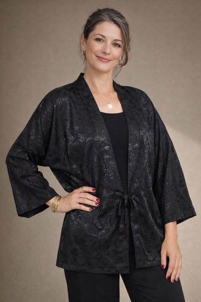 Femme souriante portant un kimono noir en satin, avec un décor neutre en arrière-plan et des accessoires dorés