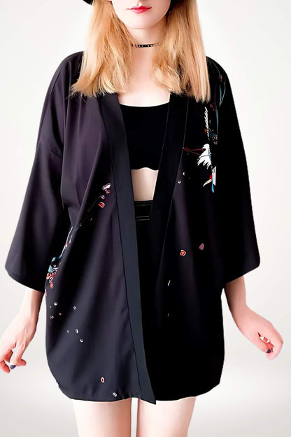 Femme portant un kimono noir avec des motifs colorés, dans une posture décontractée, sur fond clair