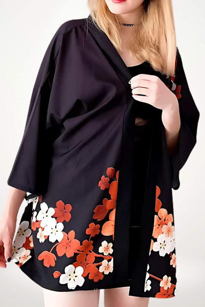 Kimono noir à motifs floraux orange et blanc, porté par une femme avec les cheveux blonds, dans un décor minimaliste