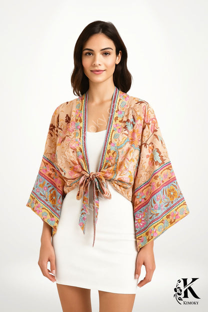 Kimono court en tissu léger aux motifs floraux colorés, porté sur une robe blanche, avec un nœud à la taille