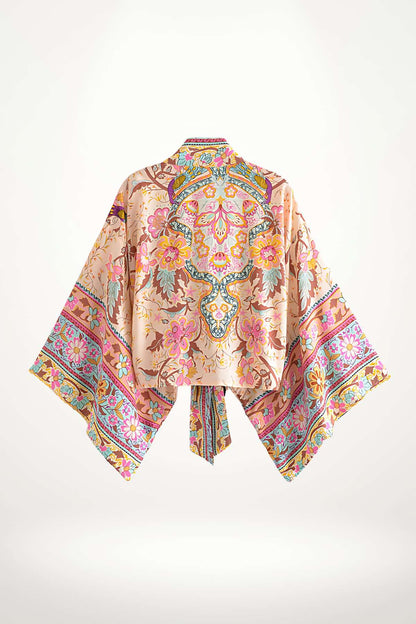 Kimono court en satin rose orné de motifs floraux colorés, avec des manches larges et un lien à la taille