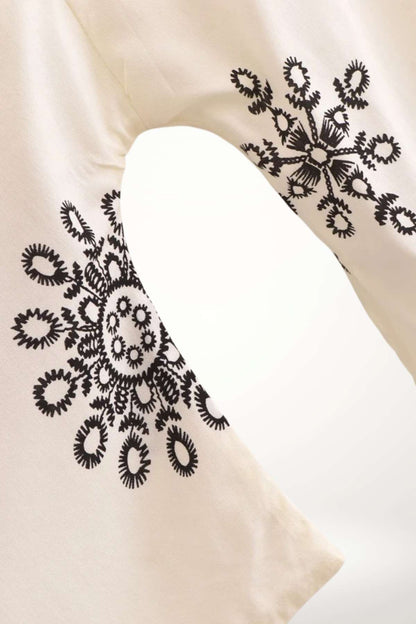 Un kimono léger en tissu crème avec des motifs floraux noirs sur les manches, évoquant un style bohème