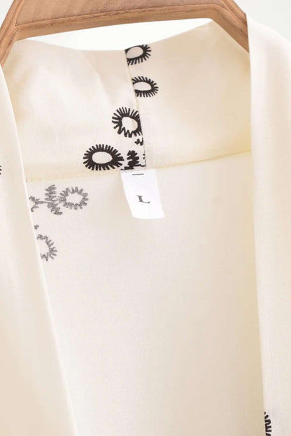 Kimono léger en tissu crème avec motifs noirs, accroché sur un cintre en bois, prêt à être porté