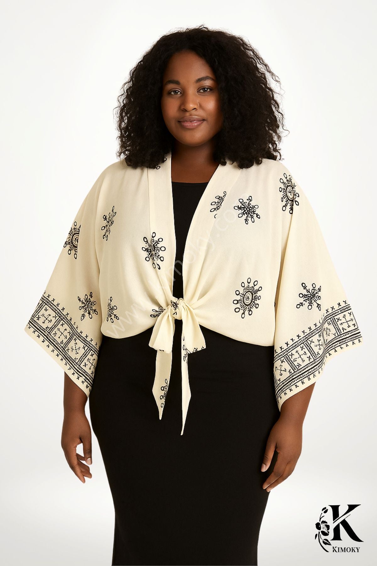 Femme souriante portant un kimono beige avec des motifs noirs, noué à la taille, devant un fond blanc